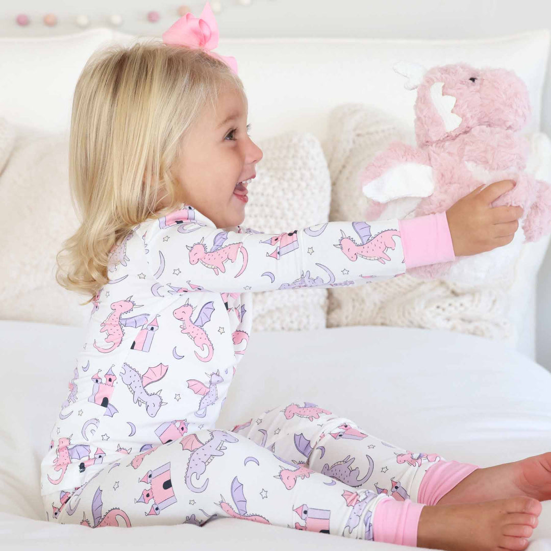 girl wearing pink and purple dragon and castle long sleeve and pants pajama set holding a pink dragon stuffed animal 