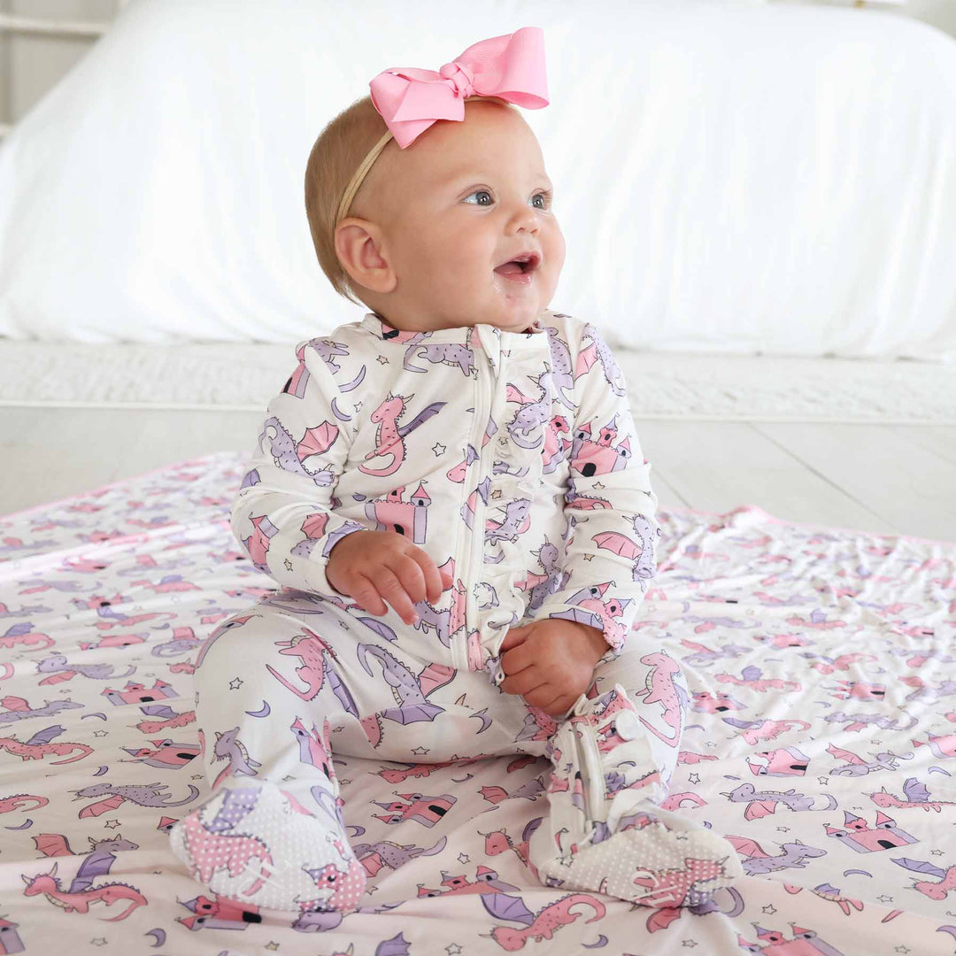 baby girl sitting wearing a pink and purple dragon and castle ruffle zipper footie with pink ribbon bow headband 