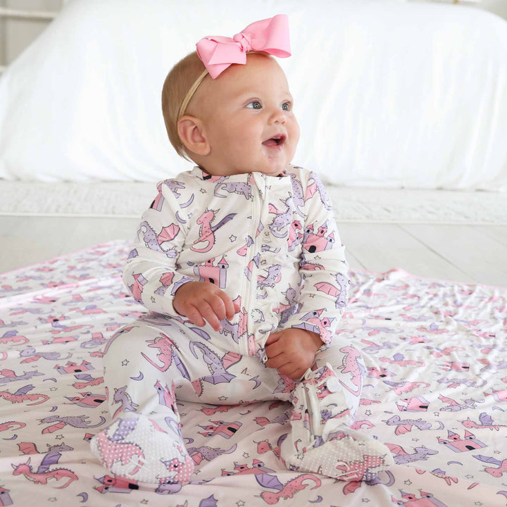 baby girl sitting wearing a pink and purple dragon and castle ruffle zipper footie with pink ribbon bow headband 