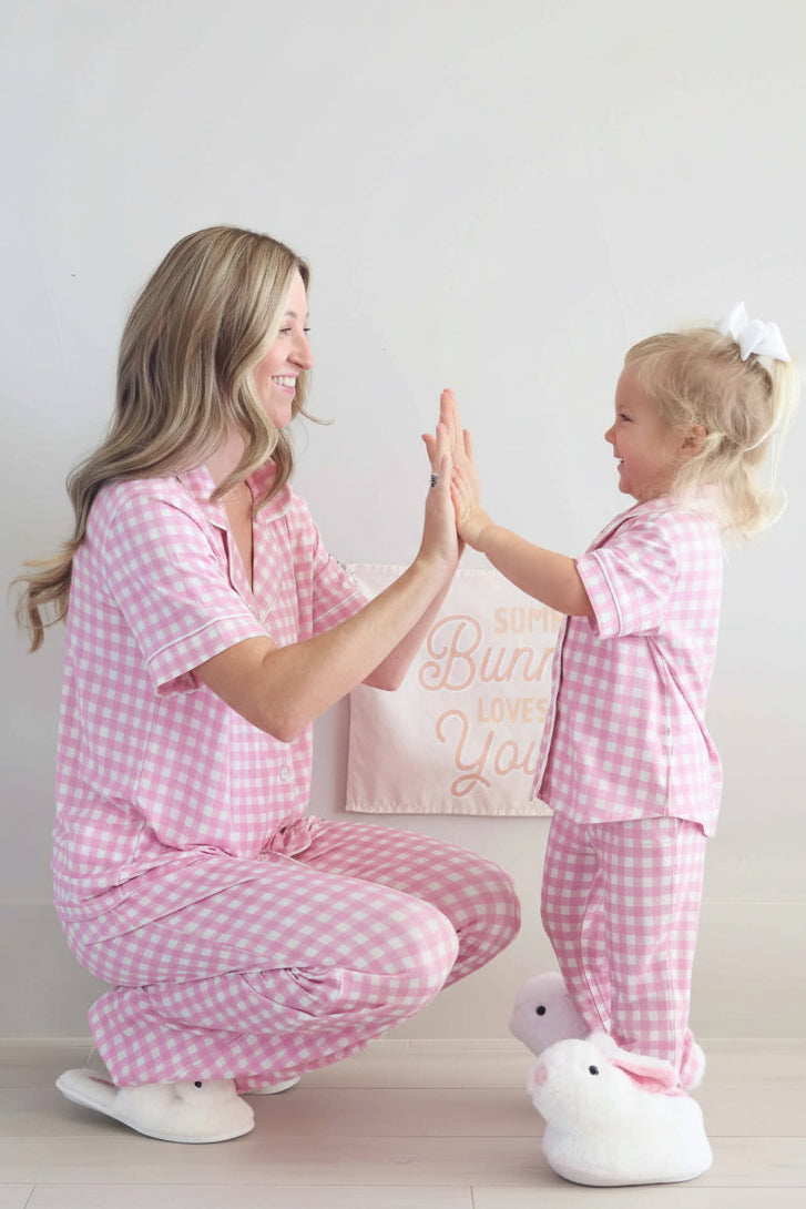 mom squatting down in pink gingham short sleeve lounge set high fiving girl in matching set wearing bunny slippers 