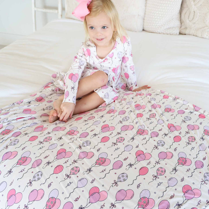 girl sitting on pink balloon bamboo blanket wearing a matching dress