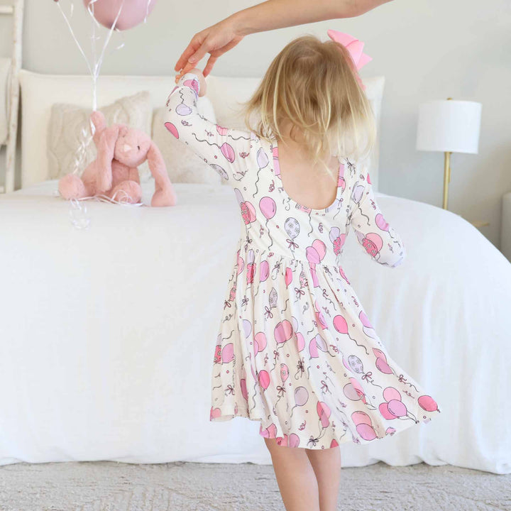 girl wearing a long sleeve birthday-themed dress and twirling 
