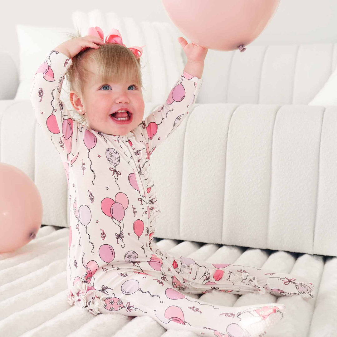 baby girl wearing a pink and purple balloon ruffle footie pajama holding a pink balloon 