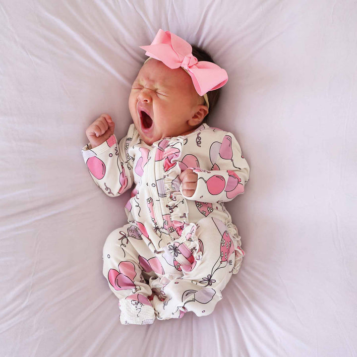 yawning baby wearing a pink balloon ruffle zipper footie with matching solid pink ribbon bow headband 