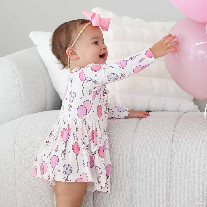 toddler girl wearing a long sleeve bodysuit with skirt with pink balloons and streamers on it for birthday