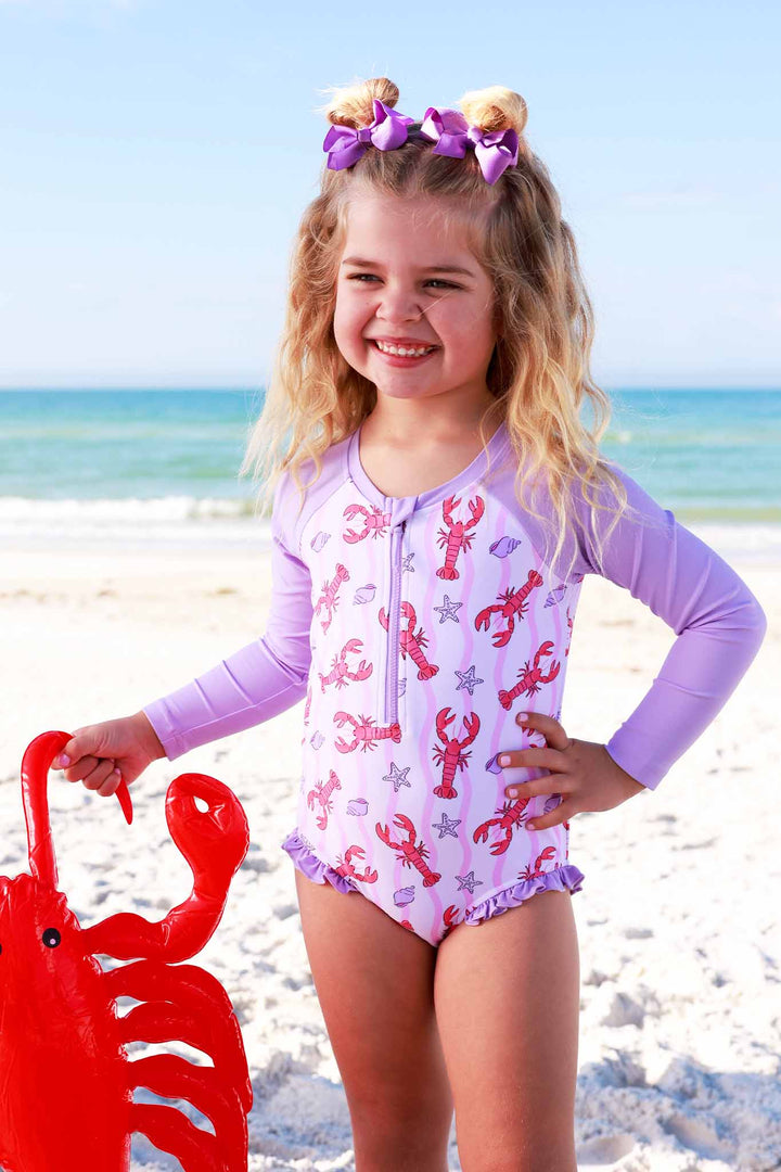 girl standing on the beach in long sleeve rash guard swim suit with lobsters holding an inflatable lobster 