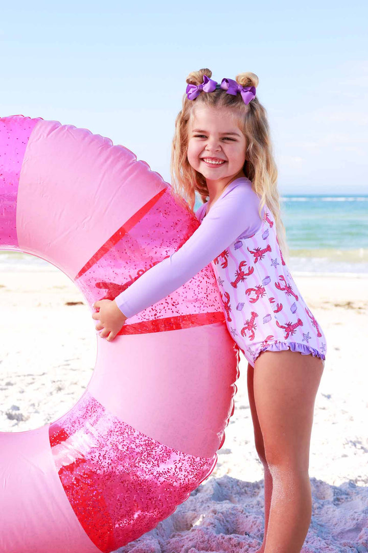 girl holding a pink innertube at the beach in pinch me long sleeve rash guard swimsuit with front zipper 