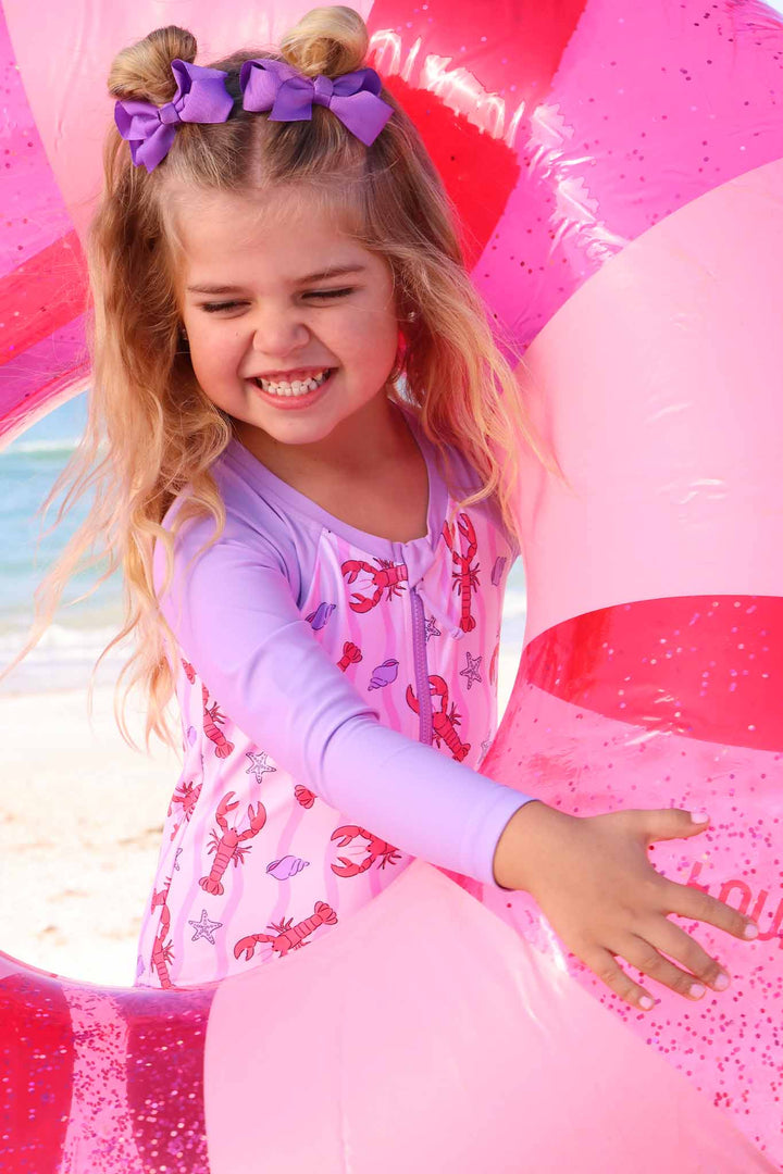 girl wearing pinch me long sleeve rash guard swimsuit standing in pink innertube with space buns 