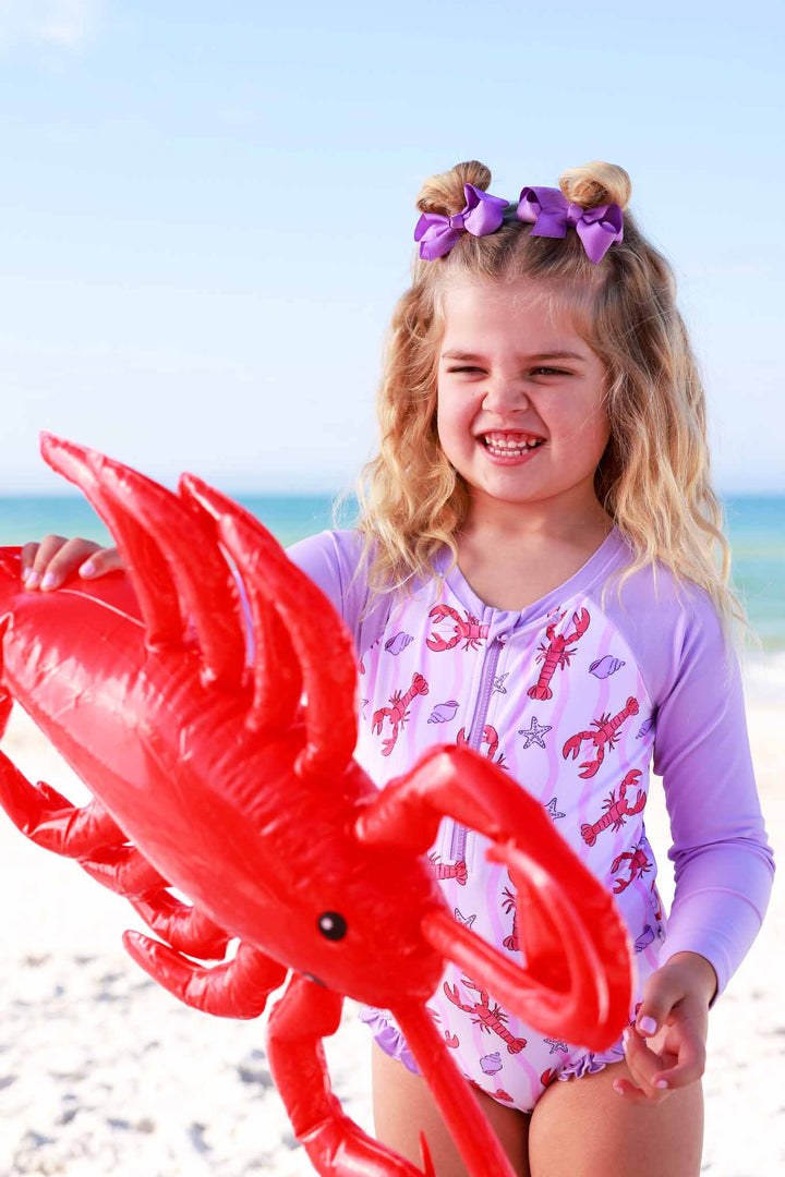 girl playing with inflatable lobster wearing a lobster rash guard swimsuit 