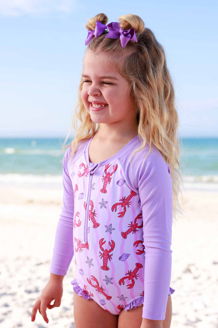 smiling girl on the beach in long sleeve rash guard swimsuit with lobsters, seashells and starfish 