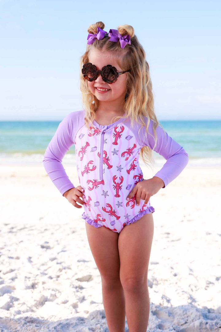 girl standing on the beach with her hands on her hips in pinch me long sleeve rash guard swimsuit 