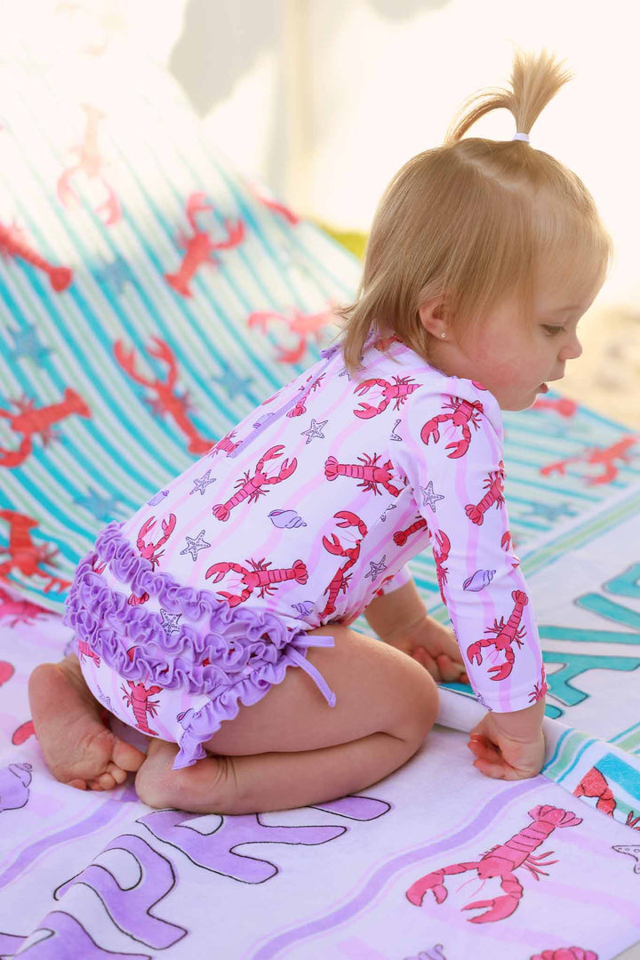 baby girl sitting on beach chair in long sleeve rash guard swimsuit with lobsters 