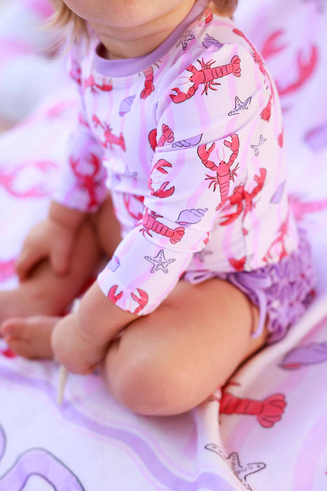 closeup of pinch me pink long sleeve rash guard swimsuit with purple ruffles on the bottom 