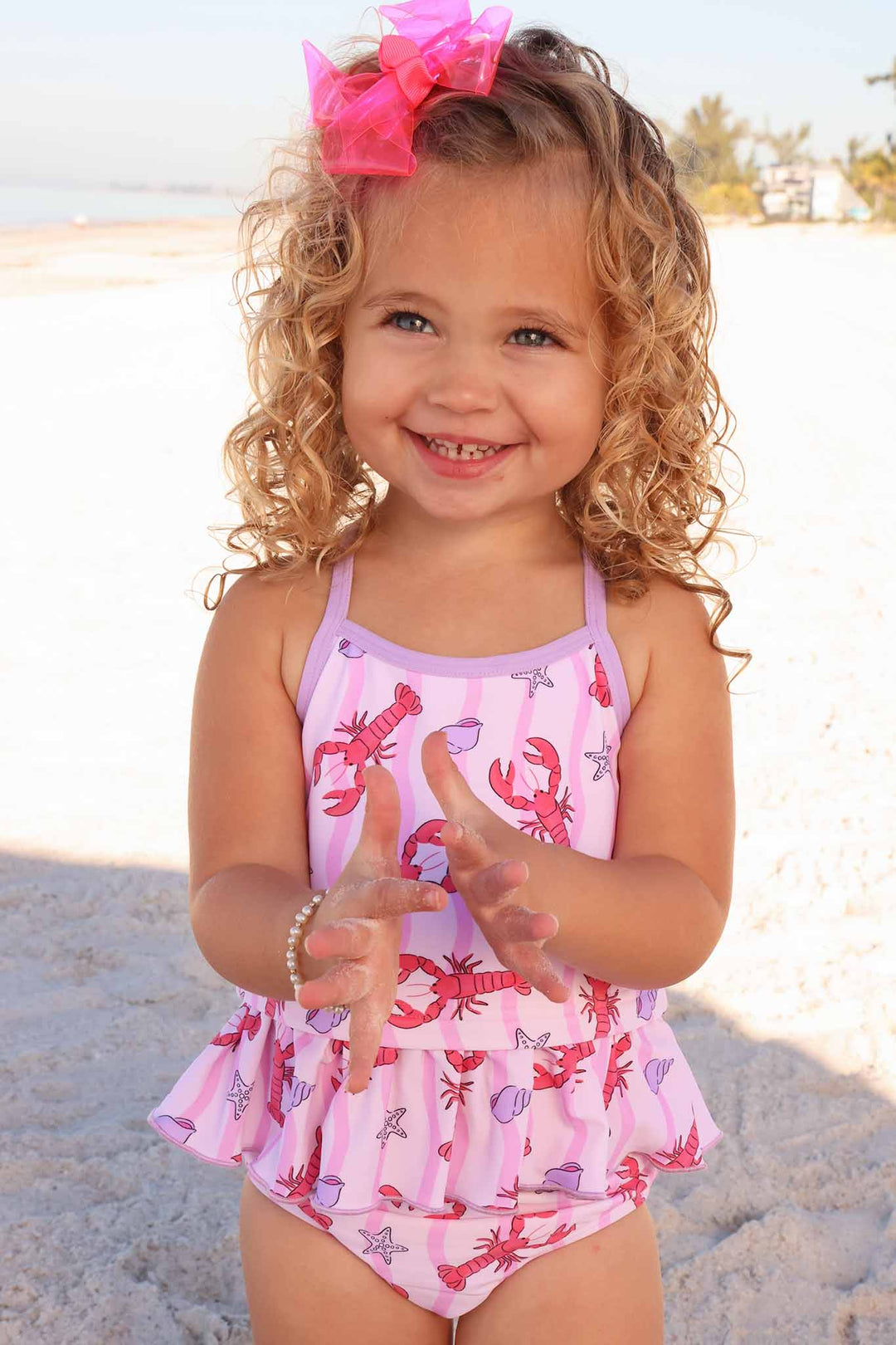 girl standing on beach clapping wearing a two piece tankini swimsuit with lobsters on it 