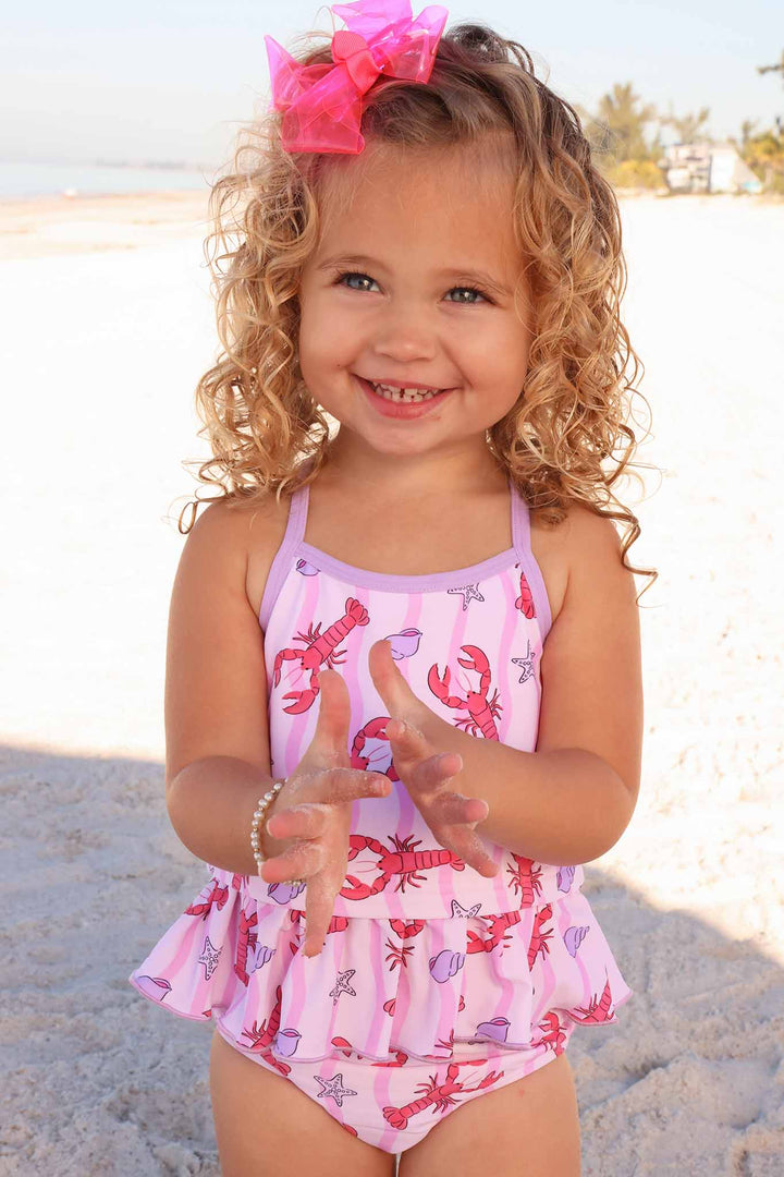 girl standing on beach clapping wearing a two piece tankini swimsuit with lobsters on it 