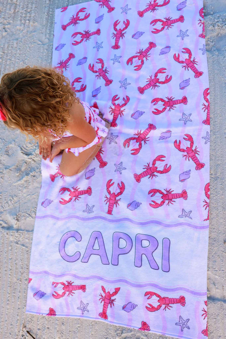 girl sitting on personalized lobster, seashell and starfish towel on beach