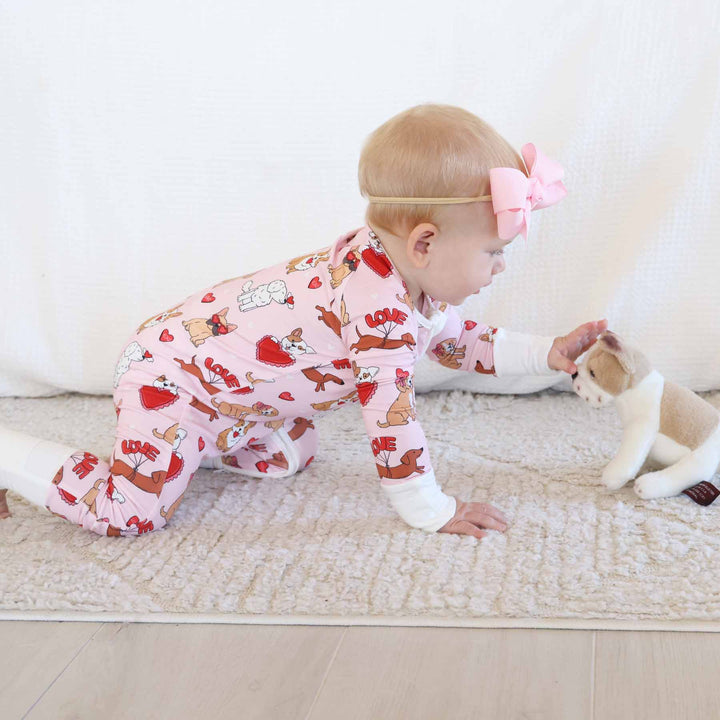 baby wearing a valentine's day dog and heart themed convertible zip romper crawling towards a puppy stuffed animal