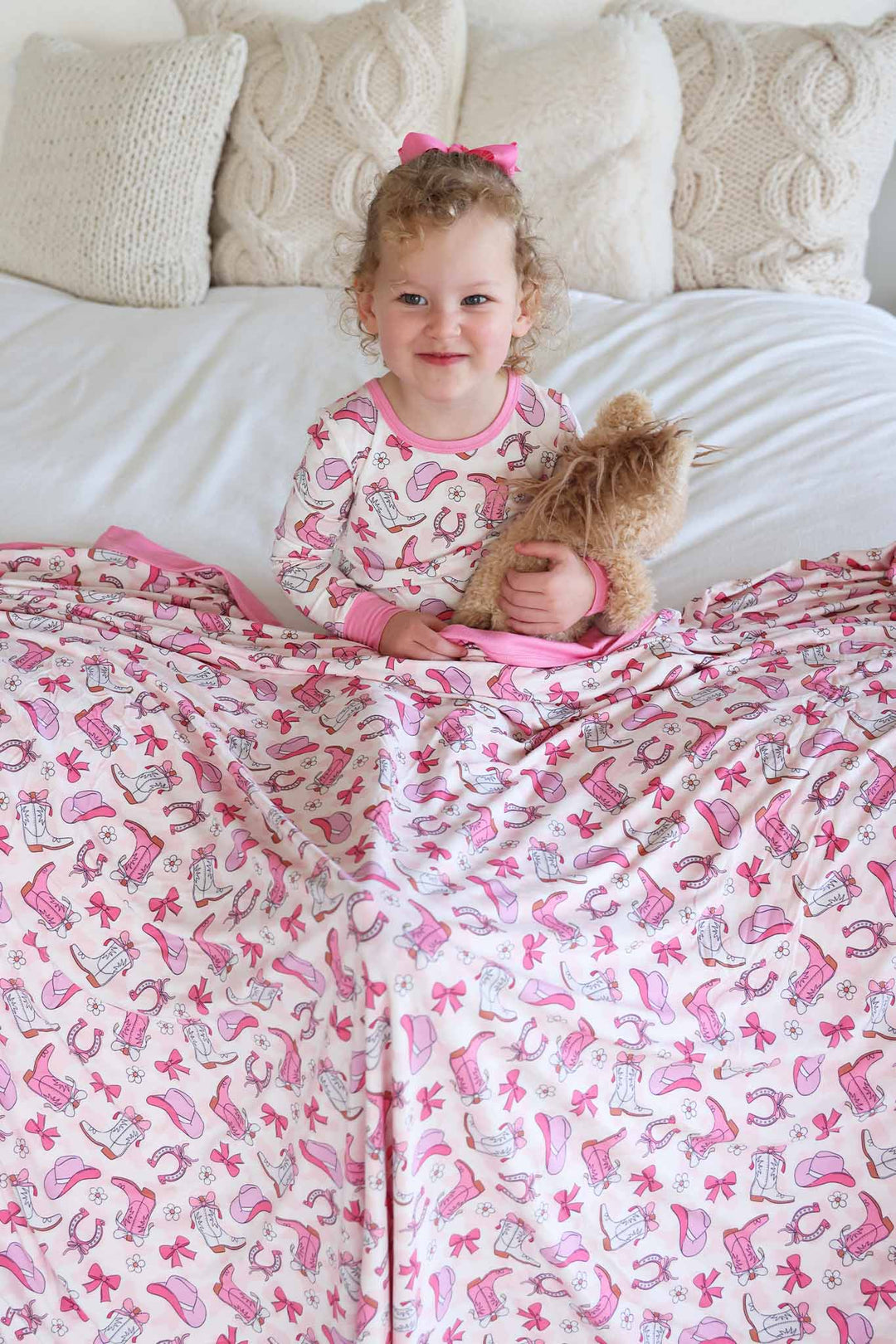 girl wearing pink rodeo dreams two piece pajama set with a matching bamboo blanket over her lap holding a horse stuffed animal 