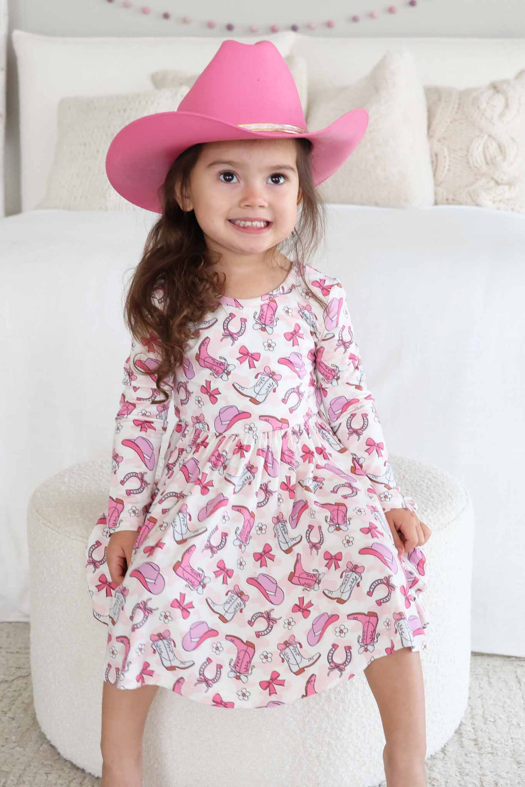girl sitting on ottoman in pink rodeo dreams twirl dress and pink cowgirl hat 