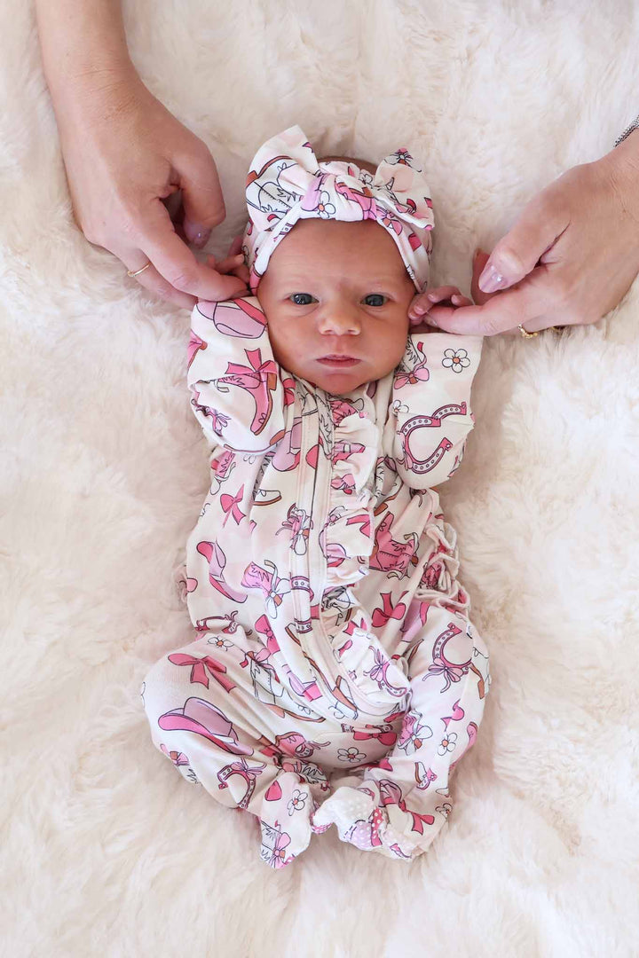newborn baby girl laying on blanket in pink rodeo themed footie pajama with ruffles 