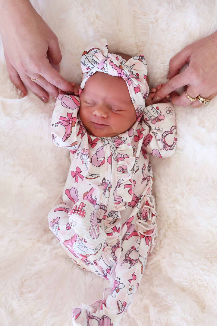 newborn girl in pink rodeo dreams ruffle zipper footie with matching headwrap