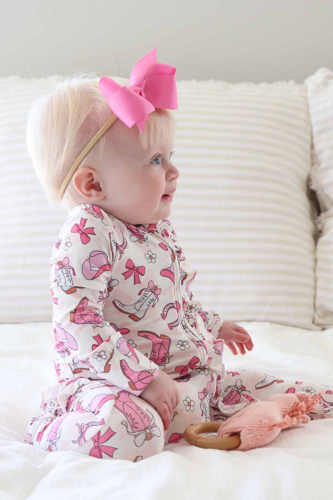 kneeling baby girl in girly western pajama footie with cowgirl boots, hats, horseshoes and daisies in pink 