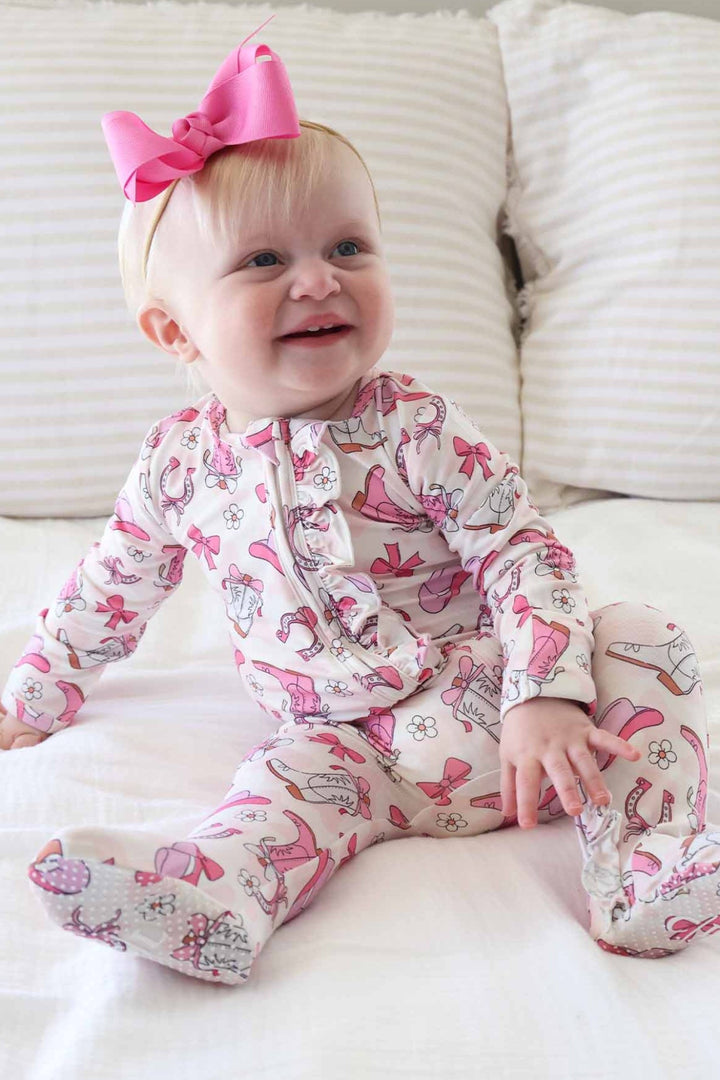 Baby wearing a pink and white outfit with a bow, sitting on a white couch.