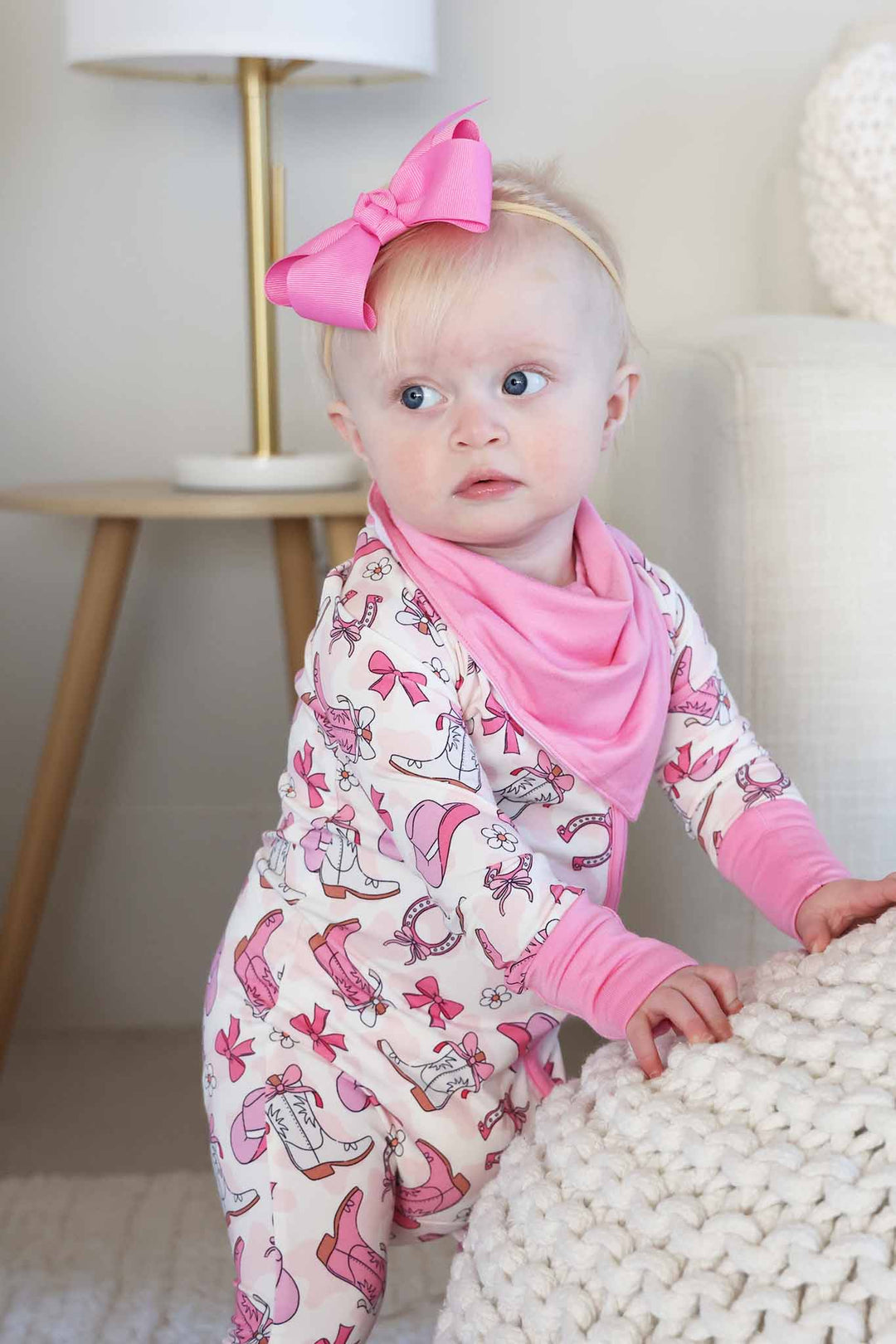 baby girl wearing the pink rodeo dreams zip romper pajama with a matching bandana bib and ribbon bow headband 