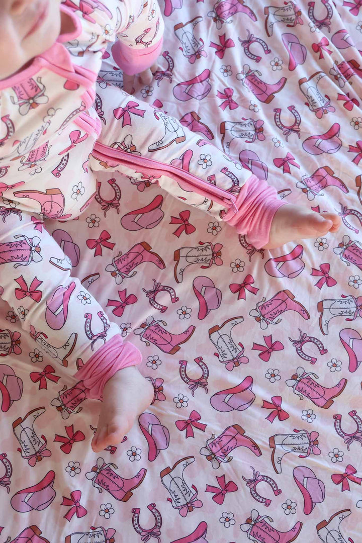 girl wearing a rodeo themed convertible zip romper pajama for girls  and sitting on a matching blanket 