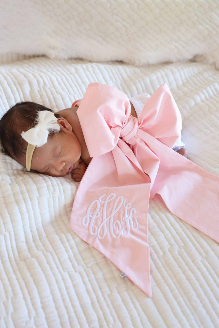 newborn girl wrapped in light pink embroidered bow sash with a white tiny velvet bow headband 