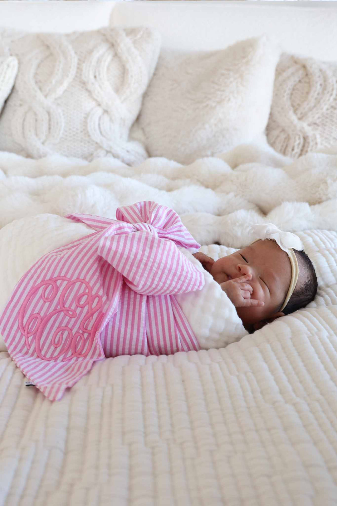 baby girl wrapped in white gauze swaddle for babies with a pink seersucker bow wrapped around her 