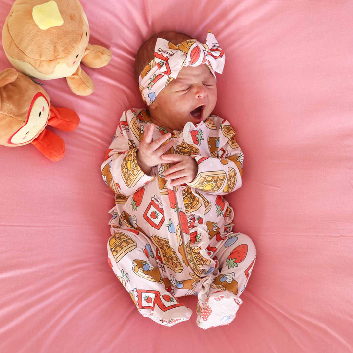 pink sweet stacks ruffle zipper footie on baby laying down wearing matching headwrap next to pancake and syrup stuffed animals 