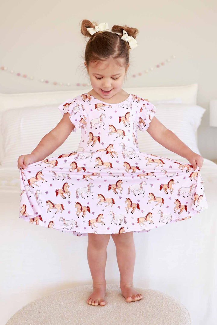 girl standing on ottoman holding out skirt on ruffle twirl dress in pony club pink print 