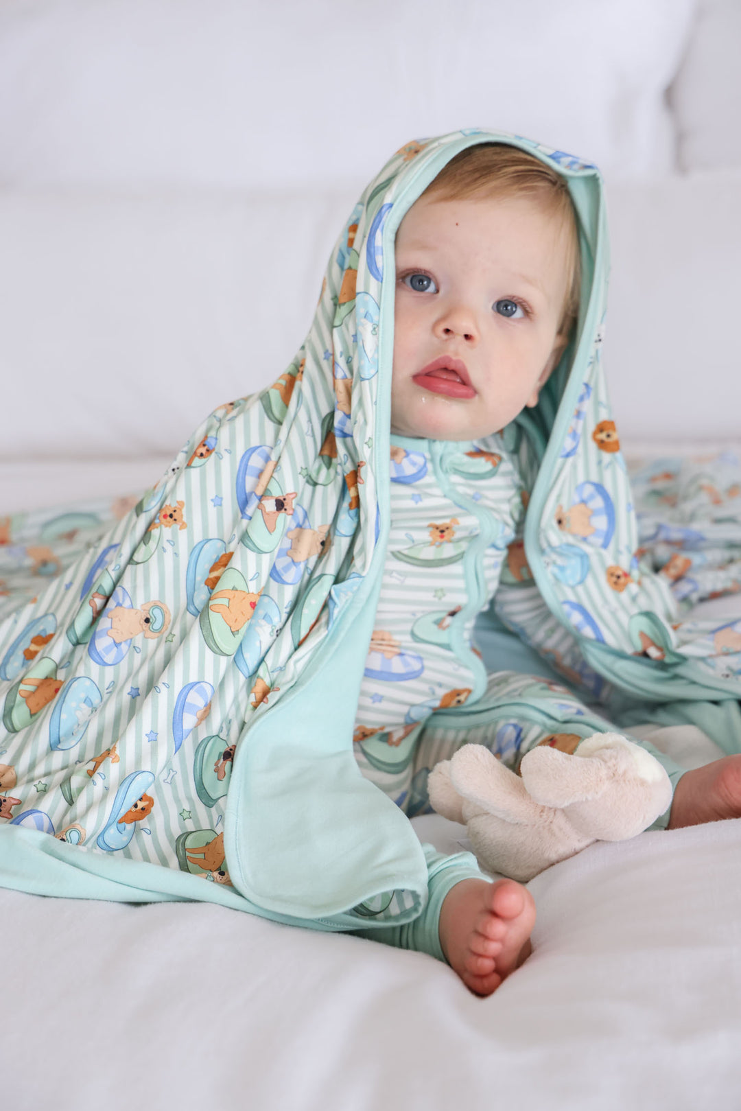 boy sitting on bed in poolside pups blue zip romper with matching bamboo blanket on his head