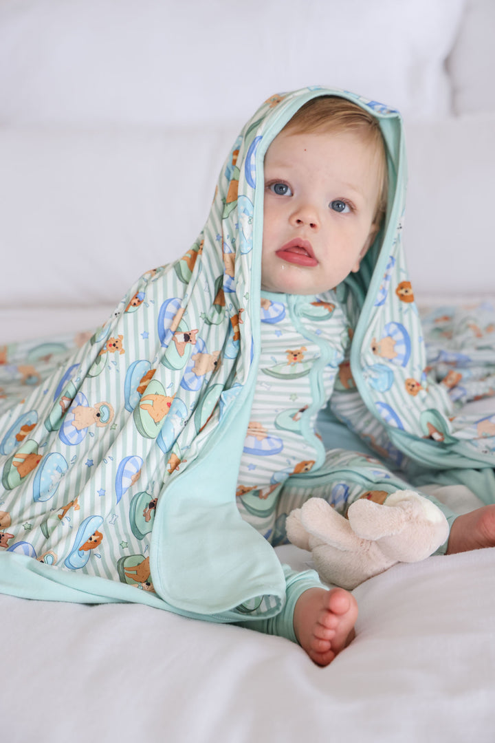 boy sitting on bed in poolside pups blue zip romper with matching bamboo blanket on his head