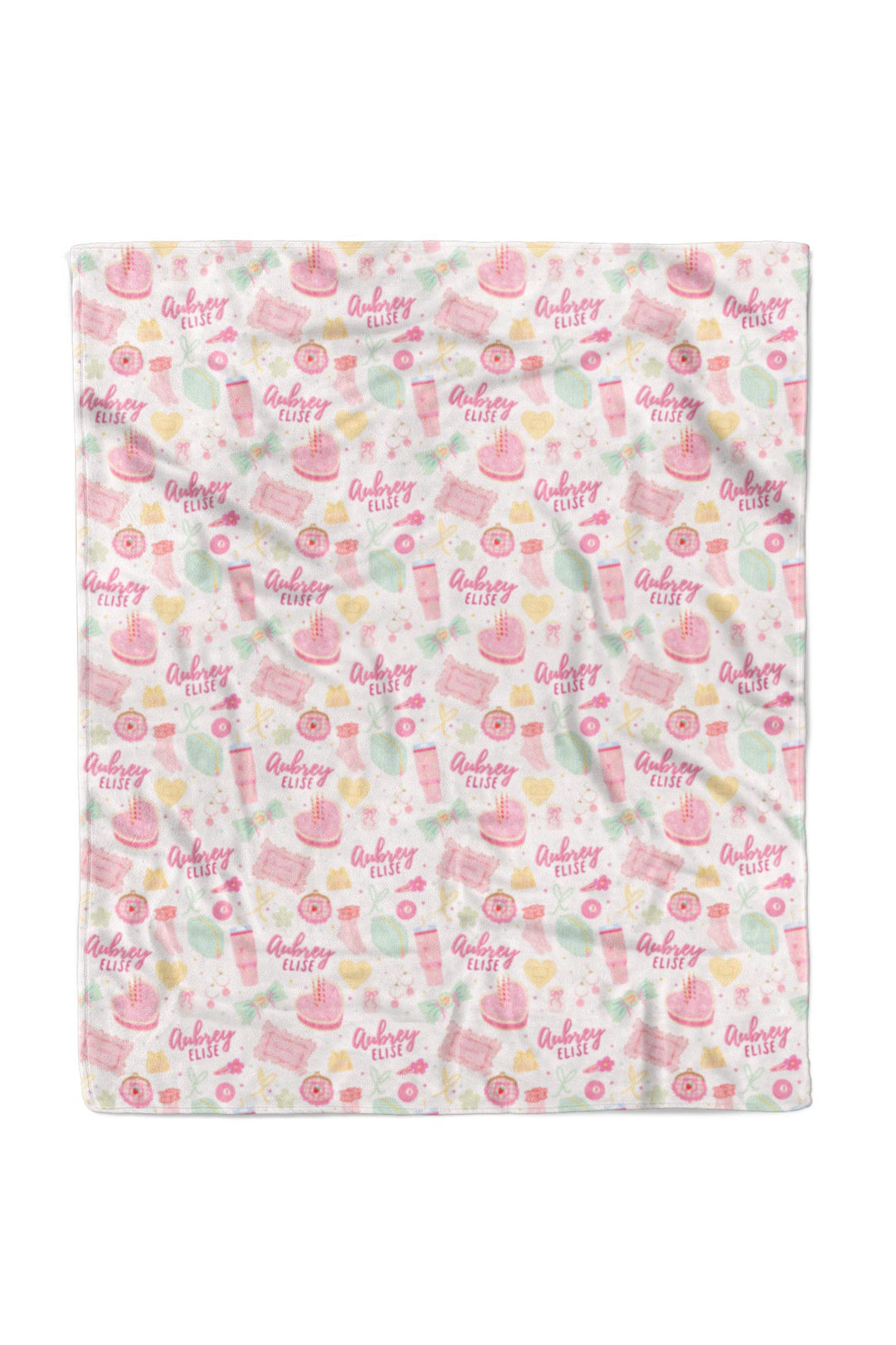 Flat lay of a fully unfolded personalized Caden Lane Pretty in Pink blanket, showing the full repeating pattern of birthday cakes, tumblers, jewelry, bows, and custom name