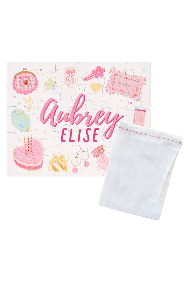 Personalized Caden Lane Pretty in Pink jigsaw puzzle in white, showing birthday cake, jewelry, and custom name, paired with a white drawstring storage bag