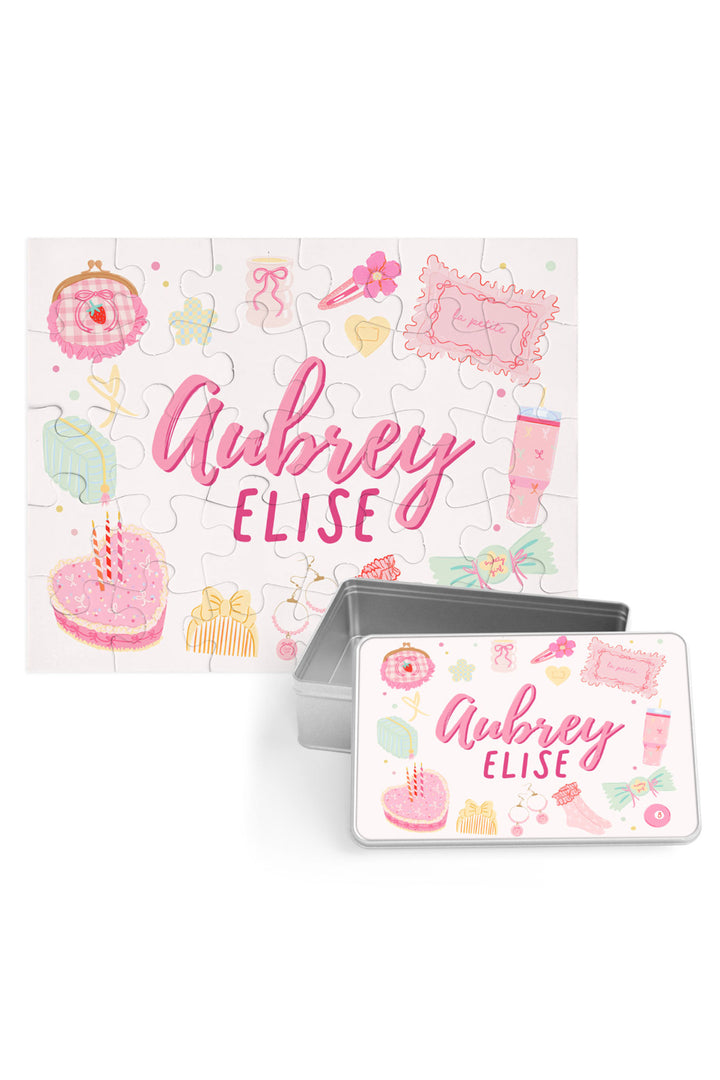 Personalized Caden Lane Pretty in Pink jigsaw puzzle in white, showing birthday cake, jewelry, and custom name, paired with a matching silver storage tin