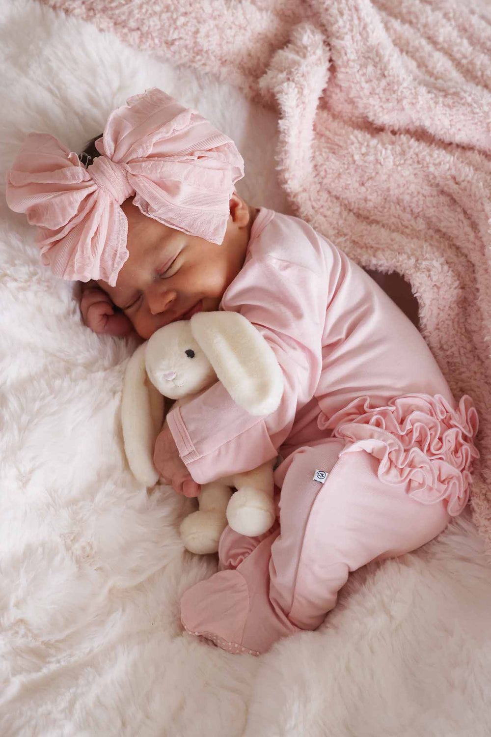 baby girl in pink ruffle footie holding mini bunny wearing matching ruffle bow