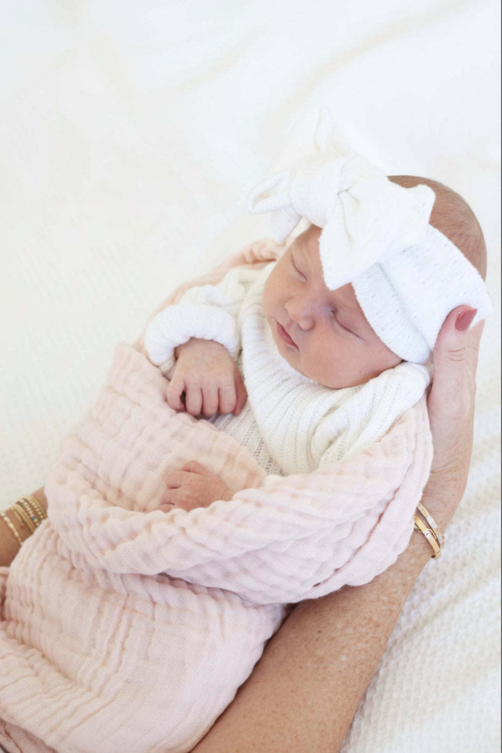 Newborn baby wrapped in a pink blanket with a white headband, held by a person.