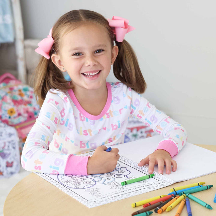 little girl smiling holding a crayon and coloring a princess themed coloring book 