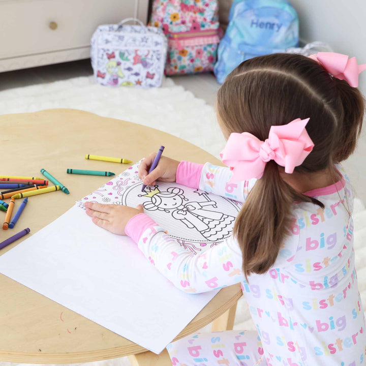 little girl sitting a table coloring a princess themed coloring book 
