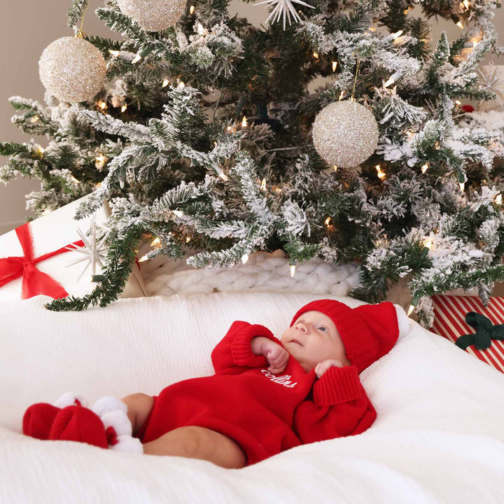 baby laying under tree with a embroidered knit sweater bubble romper with matching beanie and booties 