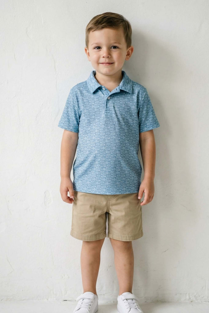 boy standing in front of white wall with fishing themed polo golf shirt on 