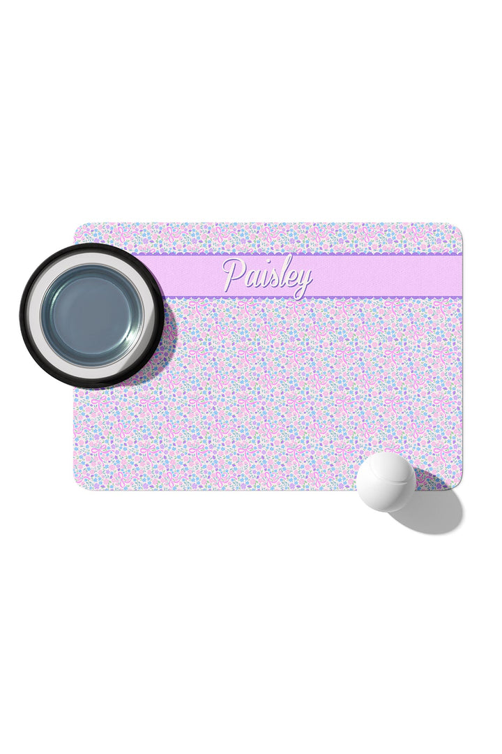 Personalized pet placemat in the Ribbon Garden print with a lavender stripe personalized with the name "Paisley", shown with a pet bowl and ball in a product mock-up