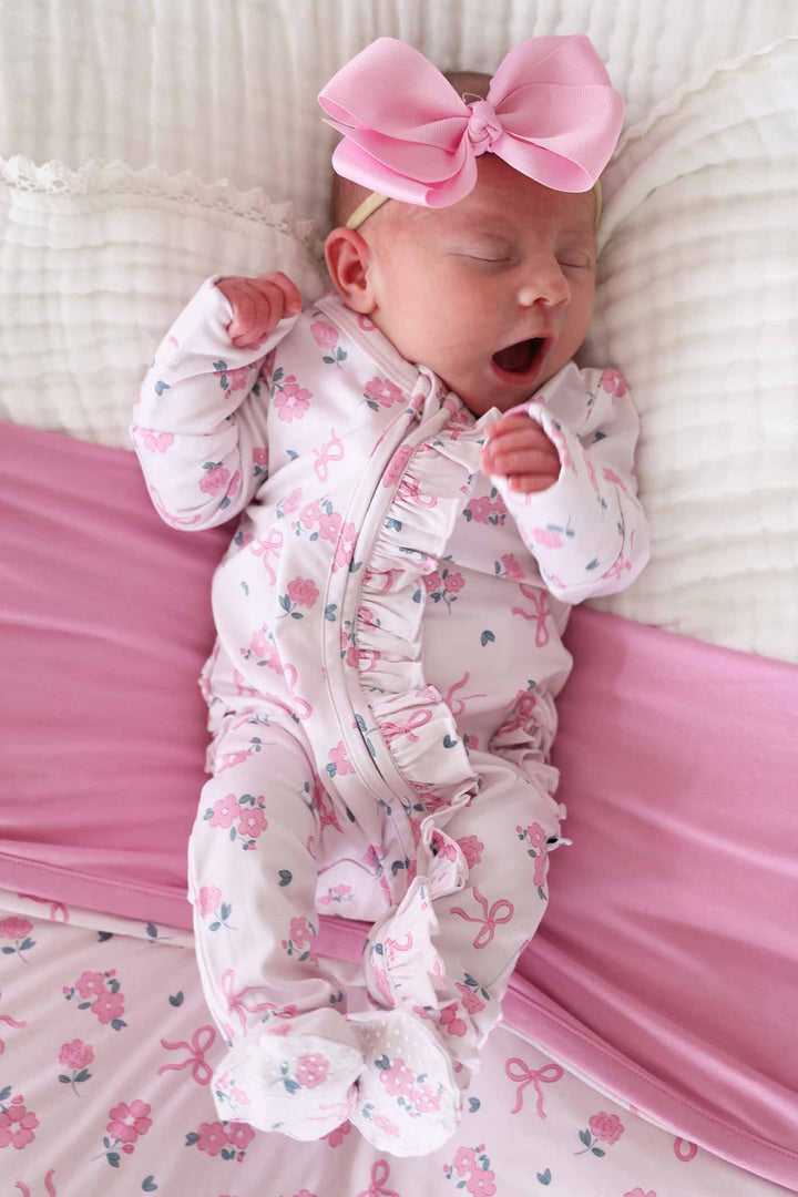 Newborn baby in a floral outfit with a pink bow on a pink blanket