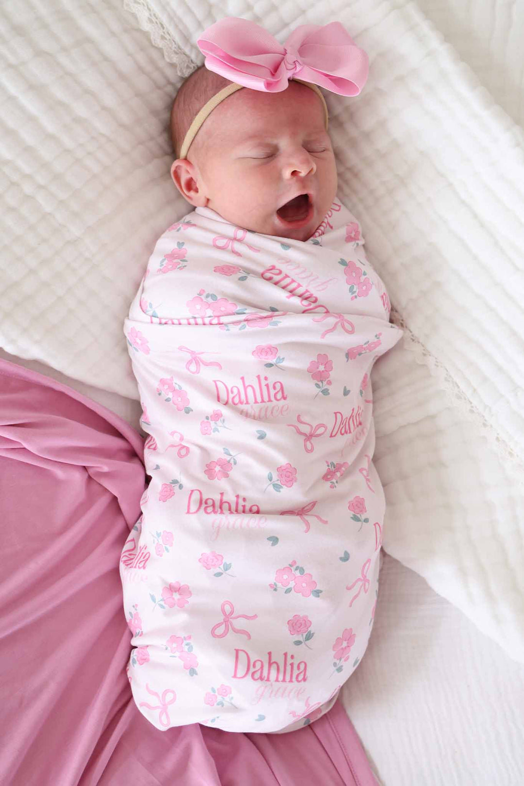 newborn wrapped in ribbon and roses pink personalized swaddle blanket with matching light pink ribbon bow headband 