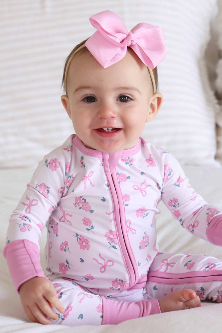 sitting baby girl with her leg out in ribbon and roses pink bamboo convertible zip romper with light pink ribbon bow headband 