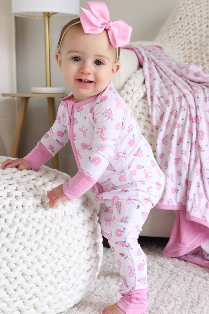 baby girl standing wearing the pink ribbon and roses convertible zip romper pajama with matching light pink ribbon bow headband 