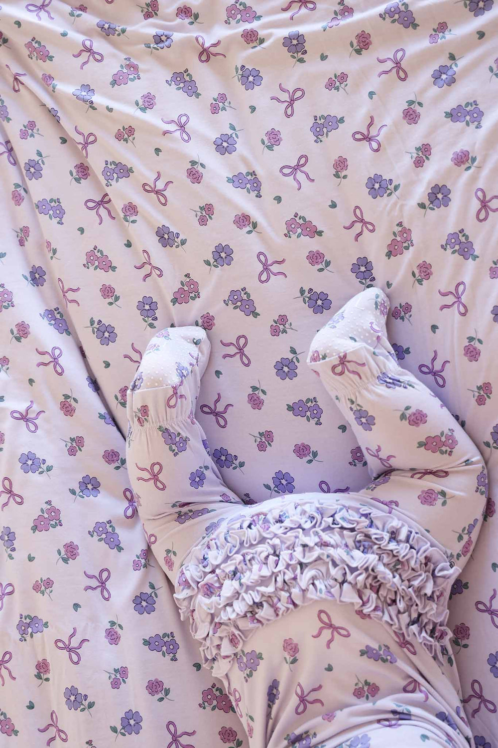 baby girl wearing purple ribbon and roses ruffle zipper footie crawling away on top of a matching bamboo blanket 